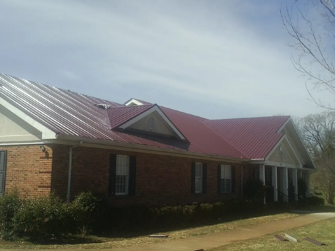 Red metal roof with gabled entries on a long brick building, from a Hail Damage Roof Repair job in Granite
