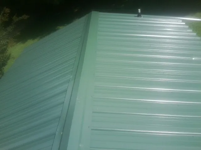 New green metal panels meeting at the ridge of a roof — Flat Roof Repair work by our crew in Granite