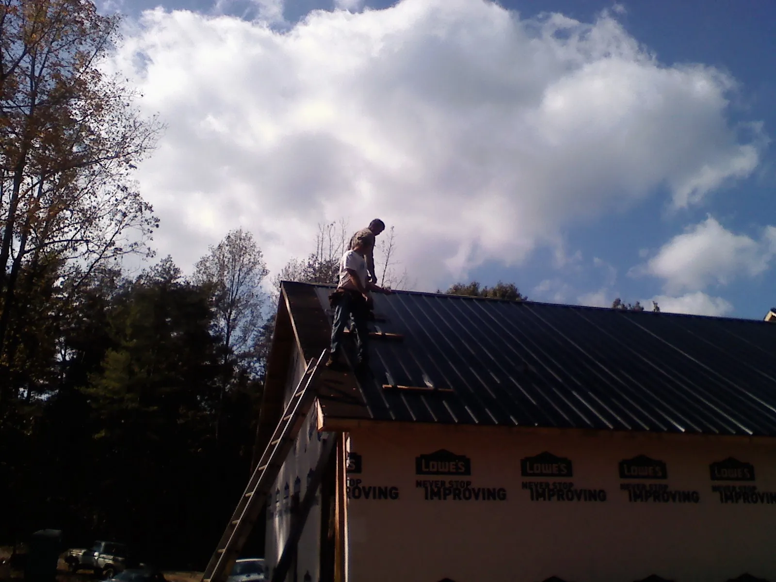 Roofer fastening dark metal panels high against a cloudy sky, from a Roof Inspection job in Granite