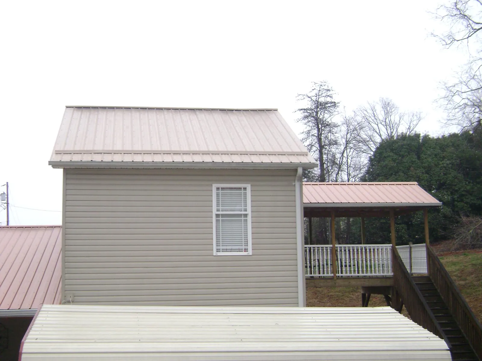 Tan metal roofs on a two story addition and attached porch, from a Roof Replacement job in Granite